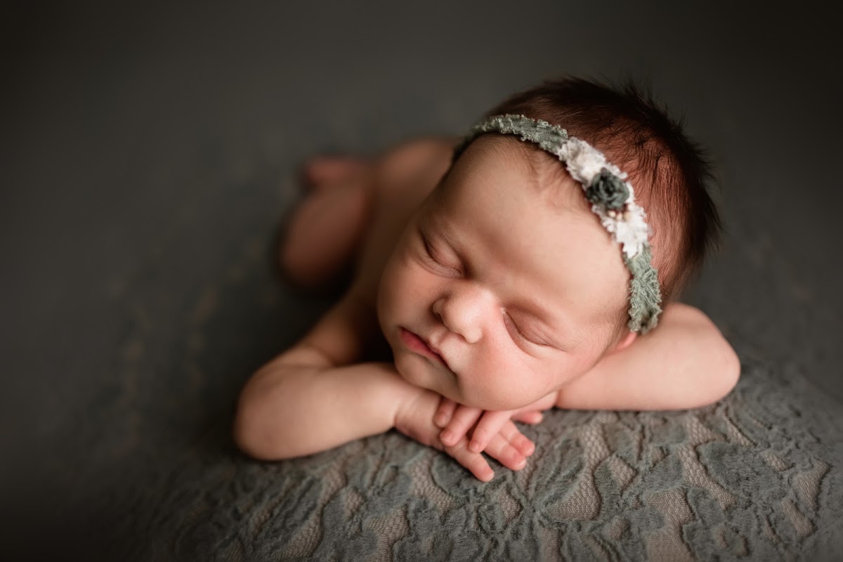 A newborn sleeping with a sage floral headband on a soft lace backdrop