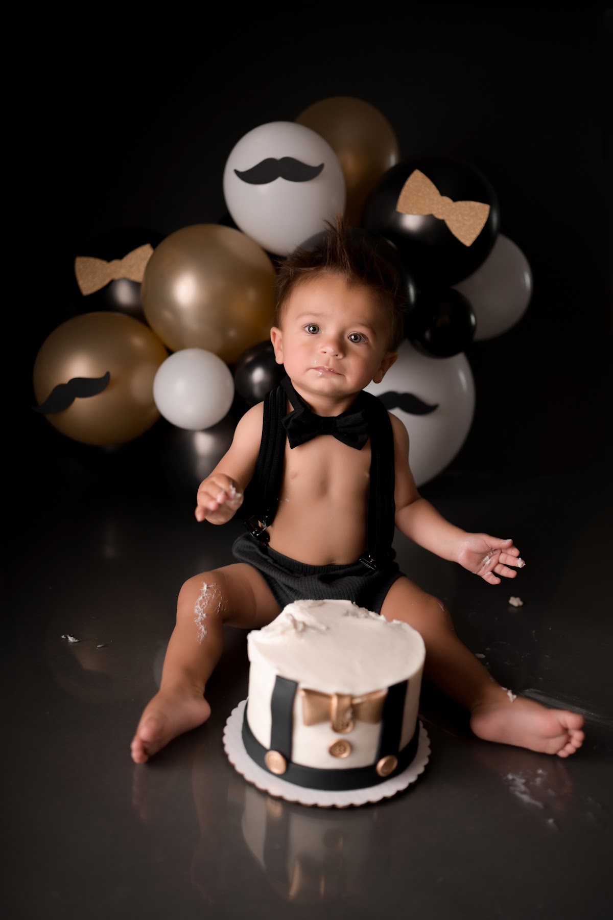 A baby boy at a black-and-gold little-man cake smash